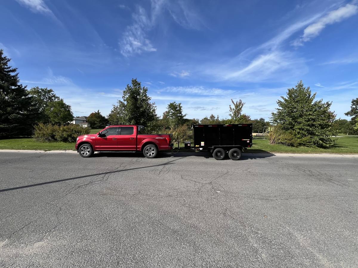 Red pickup truck towing the YGK Junk Solutions dump trailer on a Kingston street